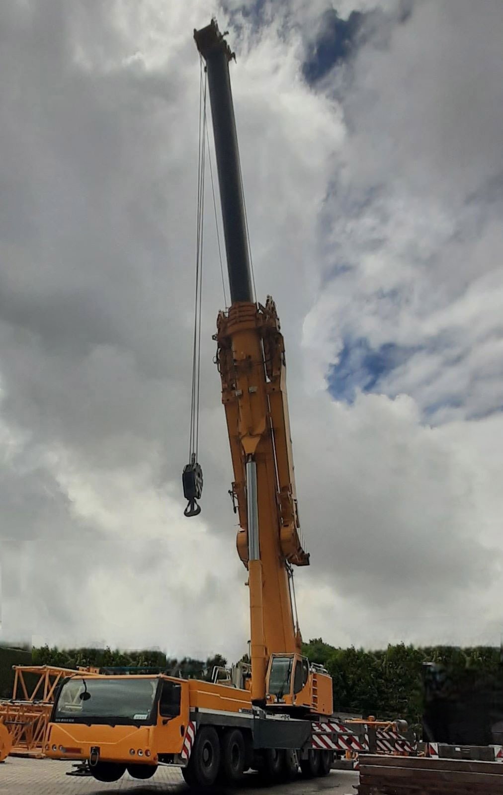 Grúa móvil todo terreno de gran capacidad, de color amarillo, con la pluma telescópica extendida casi vertical